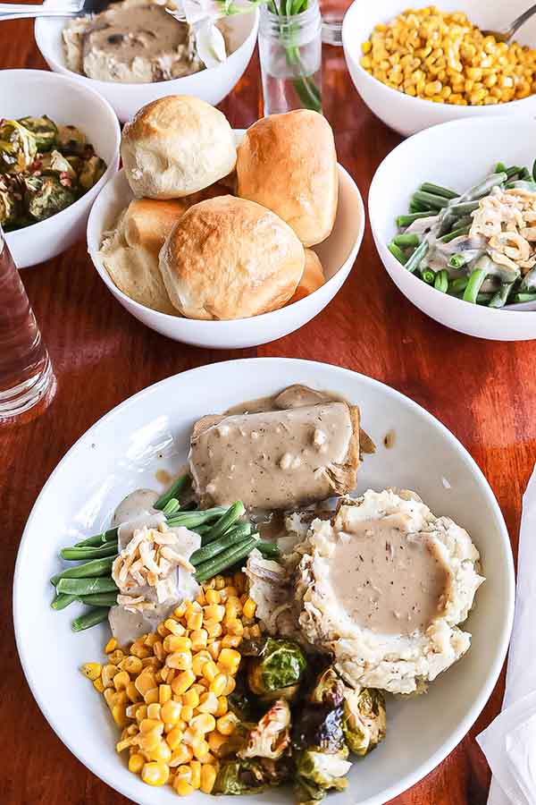 Plant-based Thanksgiving spread with mashed potatoes, gravy, green beans, corn, Brussels sprouts, and dinner rolls